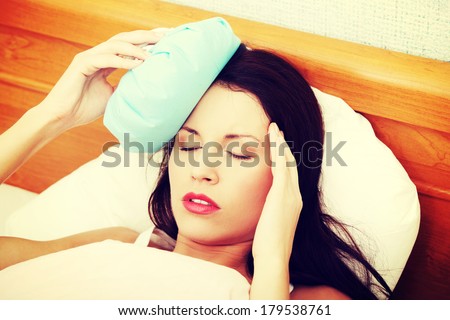 Face closeup of a young beautiful and fit woman suffering because of the headache, holding an ice-bag next to her forhead.