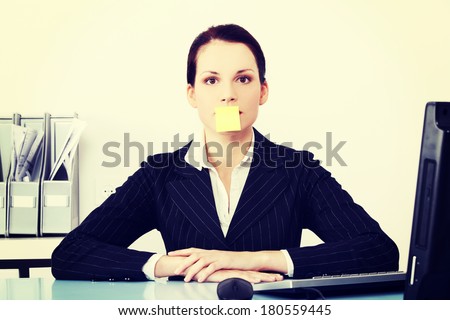 Pretty caucasian businesswoman sitting in the office with post it note on her mouth.
