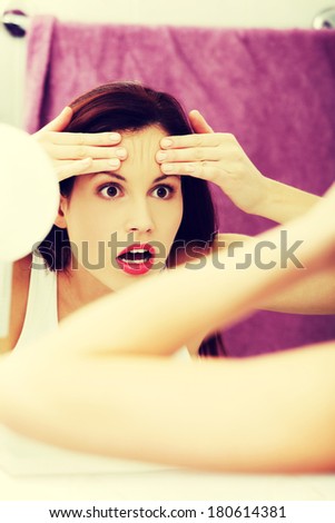 Mirror reflection of a woman worrying because of wrinkles on her forehead.