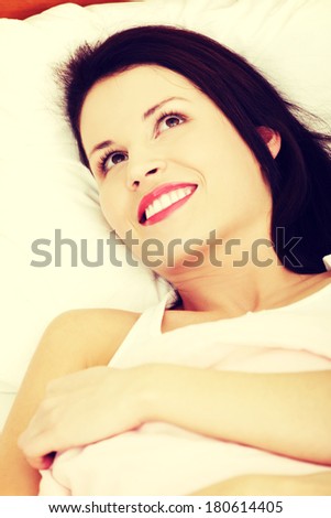 Closeup of a young beautiful smiling woman resting in the bed, looking at the right top corner.