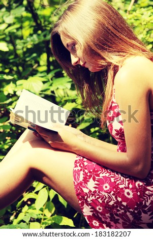 Reading woman sitting in a park bench in summer.
