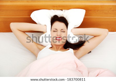 Beautiful woman is lying in bed and covering her ears with pillow. Noise or insomnia concept.