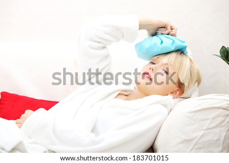 Beautiful woman is pressing ice-bag to her head, in bed. Headache concept.