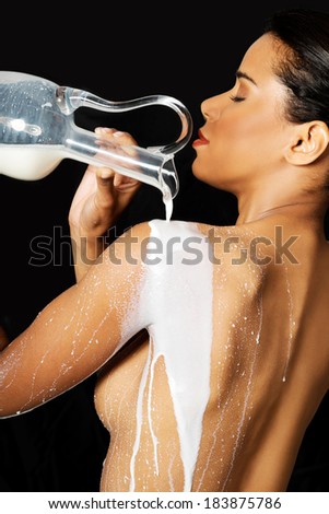 Beautiful naked woman is pouring milk on her back. On black background.