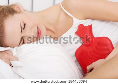 Beautiful caucasian woman lying in bed with hot water bag and holding it on her belly.