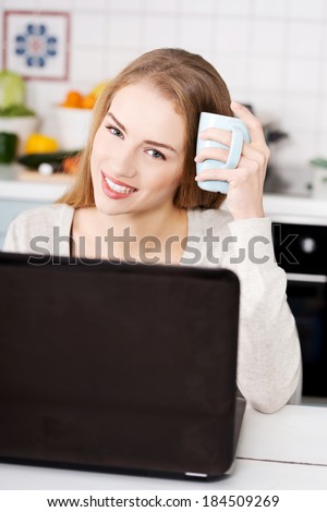 Young beautiful woman sitting by the table with laptop and cup. Kitchen background.
