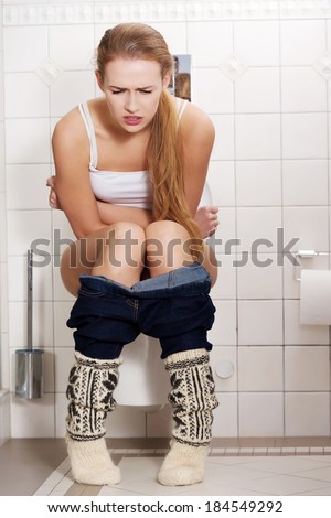 Young caucasian woman is sitting on the toilet. urinary bladder problem or pregnancy or sickness concept.