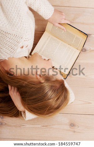 Young beautiful woman lying on the wooden floor with books.