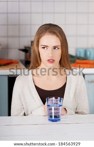 Beautiful caucasian woman sitting in the kitchen and drinking fresh water.