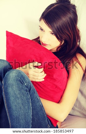 Sad woman\'s sitting on couch and squeezeing pillow.