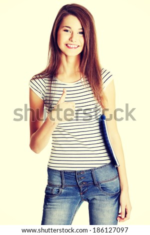 Front view portrait of a young happy female caucasian student holding a notebook and giving a thumb-up
