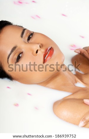 Attractive naked woman lying in a milk bath. With rose petal. Up front view.