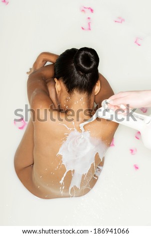 Attractive woman lying in a milk bath. Milk is spilled on her back.