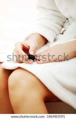 Woman is painting her fingernails with red lacquer and sitting on bed.
