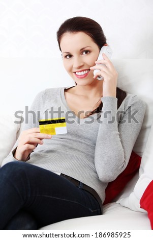 Beautiful woman is holding credit card and talking to the phone, shopping on the phone concept. Indoor.