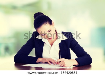 Beautiful attractive corporate lawyer business woman sitting at desk and writing blank paper page