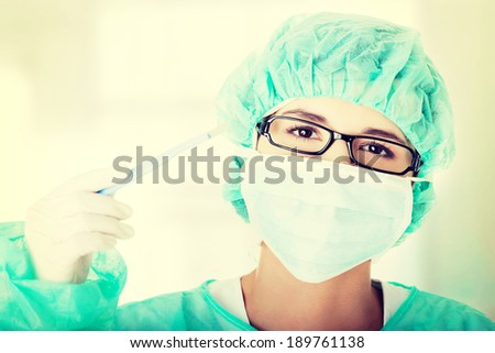 Portrait of woman doctor or nurse with surgical mask and cap holding scalpel