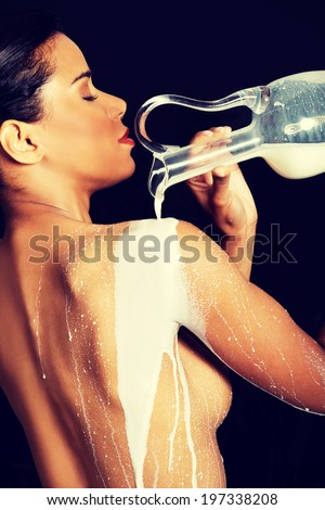 Beautiful naked woman is pouring milk on her back. On black background.
