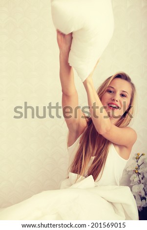 Young happy blond woman ready for pillow fight in the bed