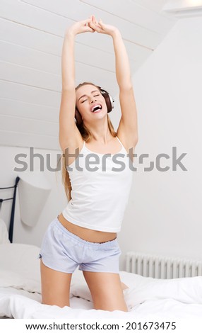 Beautiful caucasian woman in pijamas is listening to music on bed. Indoor background.