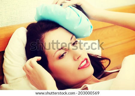 Beautiful woman is pressing ice-bag to her head, in bed. Headache concept.