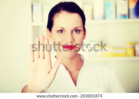 Young beautiful druggist woman is making stop sign. Health protection concept.