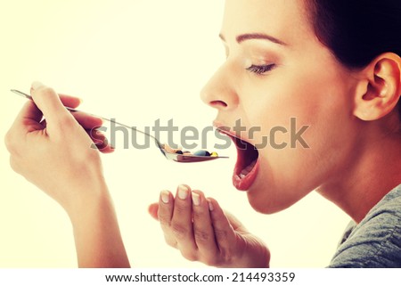 Young casual woman eating pills on a spoon. Isolated on white.