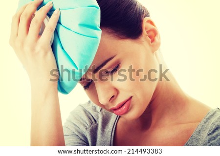 Young beautiful woman is haveng a headache and holding ice bag. Isolated on white.