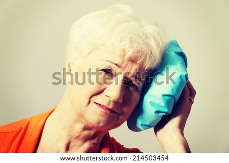 An old lady with ice bag by her head. Isolated on grey.