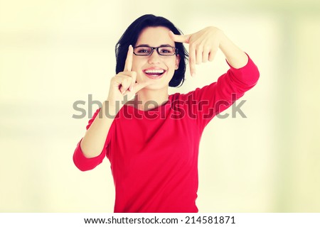 Smiling woman wearing red blouse is showing frame by hands. Happy girl with face in frame of palms. Isolated on white background.