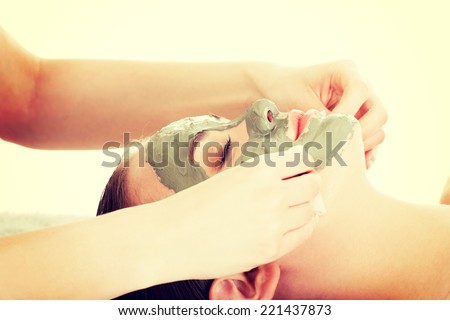 Beauty treatment in spa salon. Woman with facial clay mask. Isolated on white