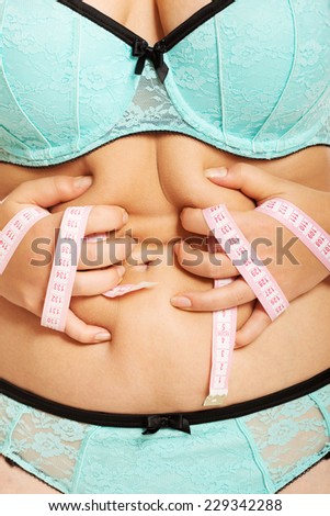 Overweight woman measuring her fat belly.