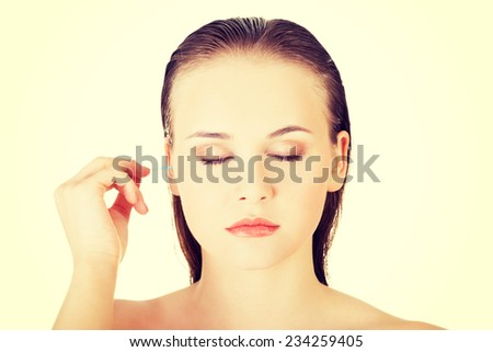 Woman face closeup while cleaning up an ear with a swab, over white.