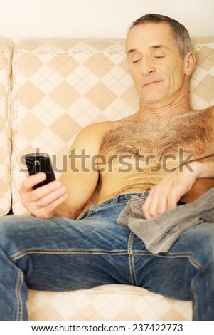 Shirtless handsome man on a sofa looking at his smartphone.