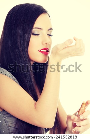 Beautiful woman applying perfume on her body, bright red perfume bottle