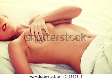 Beautiful young nude woman in bed covering her breast with hand.