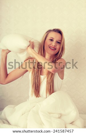 Young happy blond woman ready for pillow fight in the bed