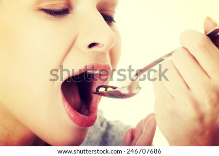 Beautiful young woman eating pills on a spoon.