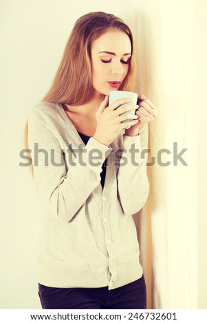 Beautiful caucasian woman standing by the window with hot drink.