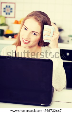 Beautiful woman sitting by the table with laptop and cup.