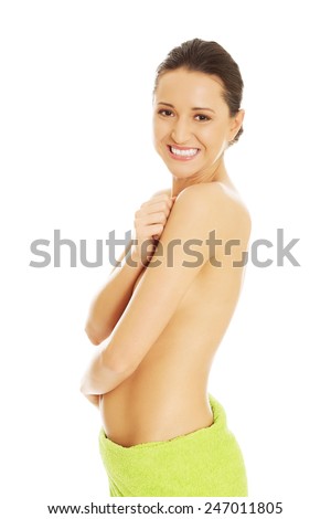 Happy smiling nude woman wrapped in towel on hips, touching her shoulder