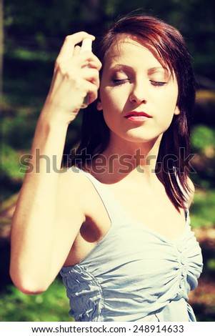 Beautiful young woman in top using spray on sun.