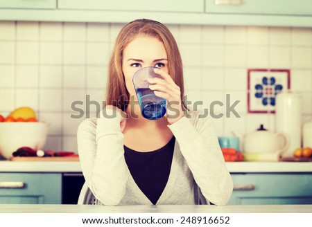 Beautiful woman sitting in the kitchen and drinking water.