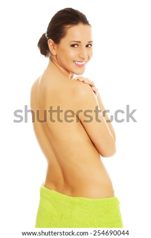 Back view of a happy smiling nude woman touching shoulder, wrapped in towel on hips