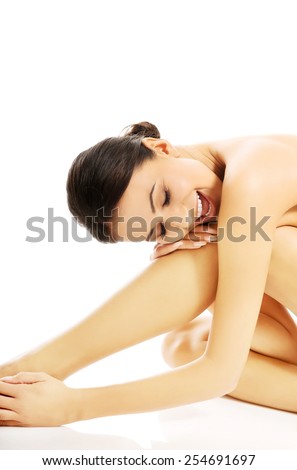 Naked slim woman sitting curled up, embracing leg