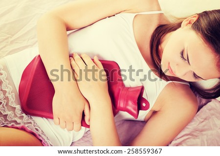 Woman lying in bed with hot water bag on belly.