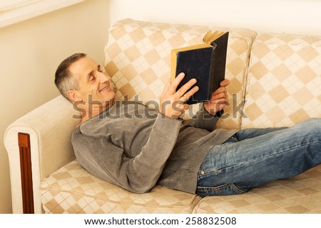 Relaxed mature man reading a book in living room.