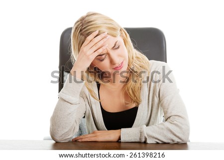 Tired woman sitting at the desk touching head.
