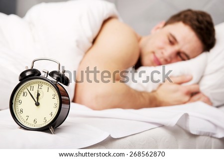 Man lying on the bed with alarm clock.