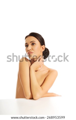 Beautiful topless woman sitting at the desk touching her neck
